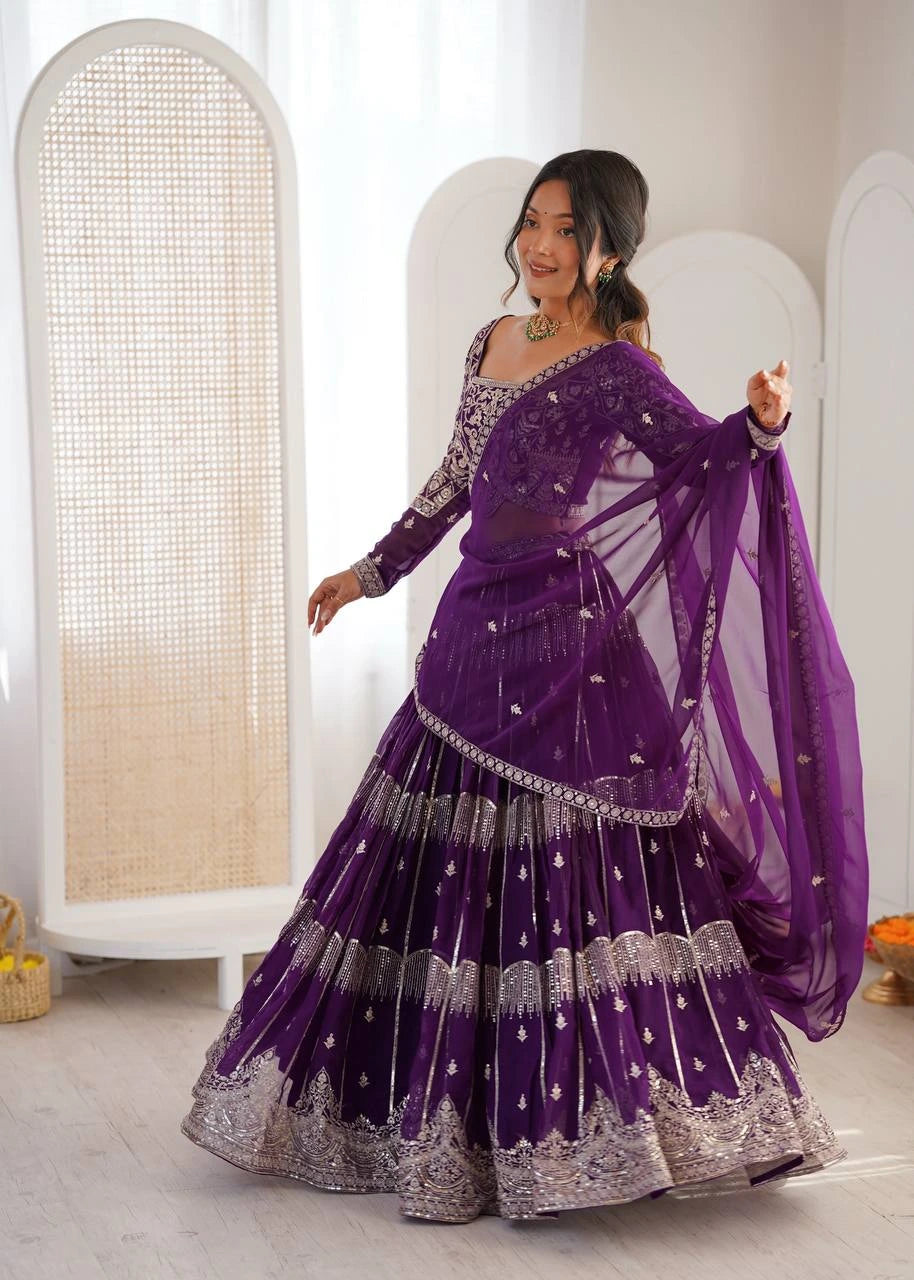 Woman in a purple traditional outfit with silver details, standing indoors.